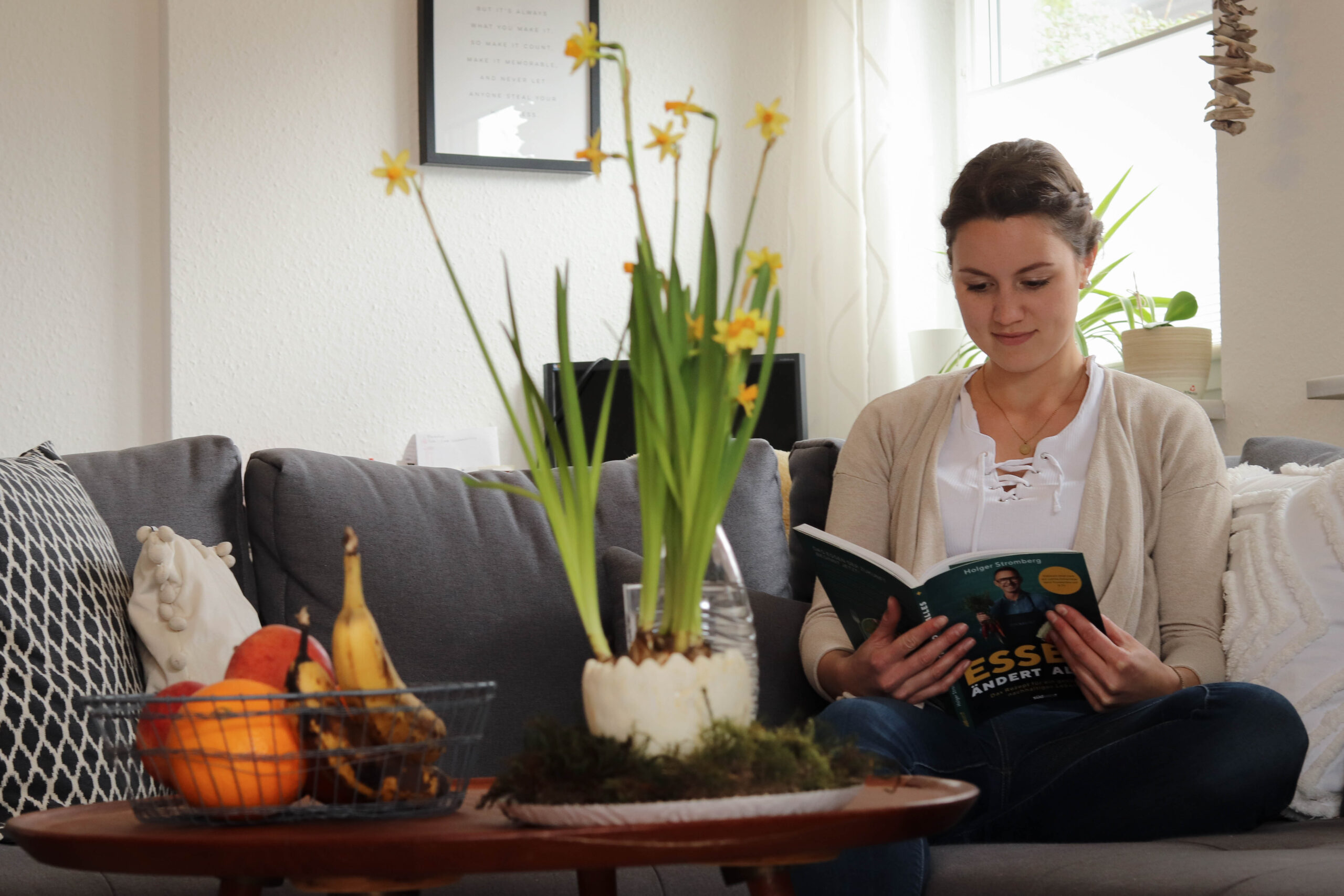 Frau sitzt auf Sofa und blättert in einem Buch.