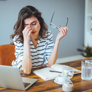 Bedeutung von Stress Eine gestresste Frau sitzt an einem Schreibtisch.